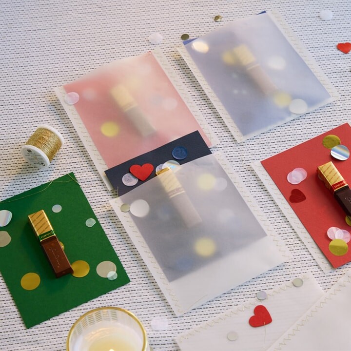 Cartes artisanales réalisées à partir de papier cartonné coloré, de papier calque, de confettis et d'un bâtonnet de chocolat merci