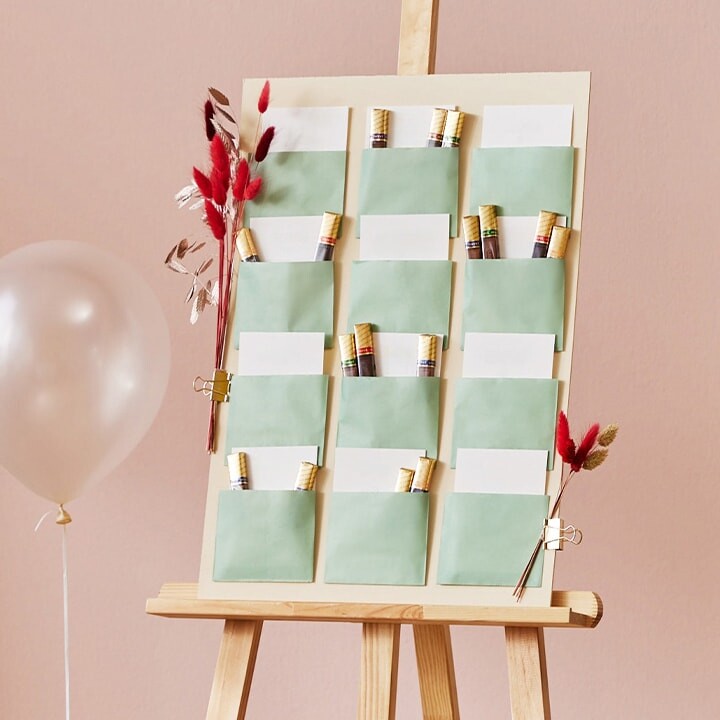 Un chevalet avec le plan de table sous forme de tableau composé d'enveloppes contenant des cartes, décoré de fleurs séchées et de ballons