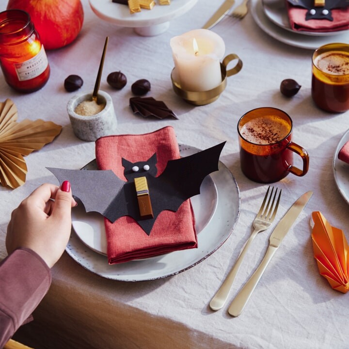 Décoration d'assiette. Chauve-souris découpée dans du carton noir, avec des yeux collés, un bâtonnet de chocolat merci